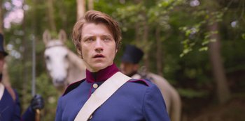 Movie still from “Ehrengard: The Art of Seduction” (2023), directed by Bille August – A man in a blue and red uniform standing next to a horse; Close Up shot, Over the shoulder angle