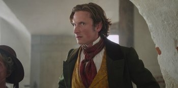 Movie still from “Ehrengard: The Art of Seduction” (2023), directed by Bille August – A person wearing a suit and tie; Close Up shot, Low angle