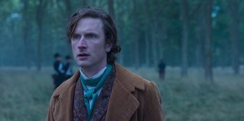 Movie still from “Ehrengard: The Art of Seduction” (2023), directed by Bille August – A man with long hair wearing a brown coat and a neck tie; Close Up shot, Over the shoulder angle