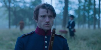 Movie still from “Ehrengard: The Art of Seduction” (2023), directed by Bille August – A man in a military uniform holding an instrument in a forest; Close Up shot, Over the shoulder angle