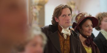 Movie still from “Ehrengard: The Art of Seduction” (2023), directed by Bille August – A man wearing a suit and a bow tie; Close Up shot, Over the shoulder angle