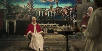 Movie still from “Ehrengard: The Art of Seduction” (2023), directed by Bille August – A man sitting in a chair in front of a painting; Wide shot, Over the shoulder angle
