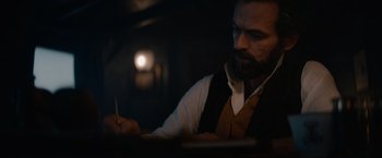 Movie still from “Eiffel” (2021), directed by Martin Bourboulon – A man with a beard writing on a piece of paper; Close Up shot, Low angle