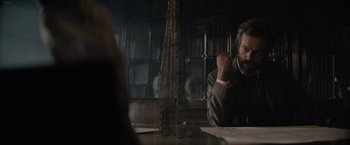 Movie still from “Eiffel” (2021), directed by Martin Bourboulon – A man sitting at a table in front of an eiffel tower; Medium shot, Over the shoulder angle