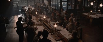 Movie still from “Eiffel” (2021), directed by Martin Bourboulon – A group of people sitting around a table with papers on top of it; Wide shot, High angle