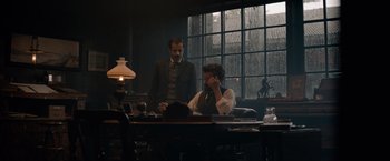 Movie still from “Eiffel” (2021), directed by Martin Bourboulon – A man sitting at a table talking on the phone; Medium shot, Over the shoulder angle