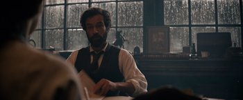 Movie still from “Eiffel” (2021), directed by Martin Bourboulon – A man sitting at a table in front of a window; Medium shot, Over the shoulder angle