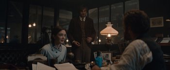 Movie still from “Eiffel” (2021), directed by Martin Bourboulon – A man and a woman standing at a table in front of a lamp; Medium shot, Over the shoulder angle