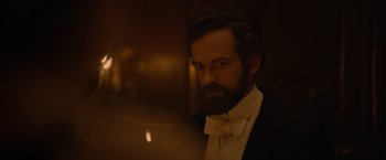 Movie still from “Eiffel” (2021), directed by Martin Bourboulon – A man with a beard wearing a suit and bow tie; Close Up shot, Over the shoulder angle