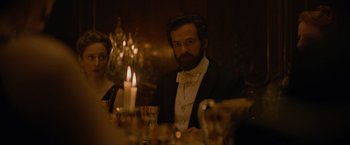 Movie still from “Eiffel” (2021), directed by Martin Bourboulon – A man sitting at a table with a candle in the background; Medium shot, Over the shoulder angle