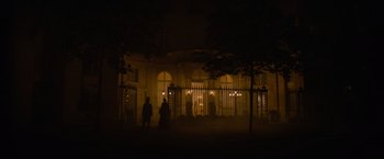 Movie still from “Eiffel” (2021), directed by Martin Bourboulon – A group of people standing in front of a building at night; Extreme Wide shot, Over the shoulder angle