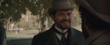 Movie still from “Eiffel” (2021), directed by Martin Bourboulon – A person wearing a suit and a hat; Close Up shot, Over the shoulder angle