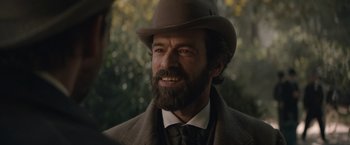 Movie still from “Eiffel” (2021), directed by Martin Bourboulon – A person wearing a hat with a beard; Close Up shot, Over the shoulder angle