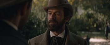 Movie still from “Eiffel” (2021), directed by Martin Bourboulon – A man with a beard wearing a hat and a suit; Close Up shot, Over the shoulder angle