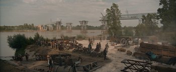 Movie still from “Eiffel” (2021), directed by Martin Bourboulon – A group of people standing next to a body of water; Extreme Wide shot, High angle
