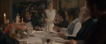 Movie still from “Eiffel” (2021), directed by Martin Bourboulon – A woman standing at a dinner table holding a plate; Medium shot, Over the shoulder angle