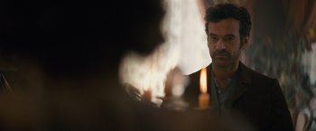 Movie still from “Eiffel” (2021), directed by Martin Bourboulon – A man sitting in front of some candles in a room; Close Up shot, Over the shoulder angle
