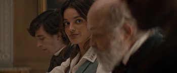 Movie still from “Eiffel” (2021), directed by Martin Bourboulon – A woman sitting in front of a group of people; Close Up shot, Over the shoulder angle