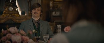 Movie still from “Eiffel” (2021), directed by Martin Bourboulon – A man sitting at a table with a glass of red wine; Close Up shot, Over the shoulder angle