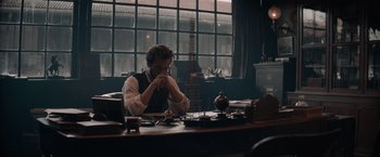 Movie still from “Eiffel” (2021), directed by Martin Bourboulon – A man sitting in front of a table in a room; Wide shot, Low angle