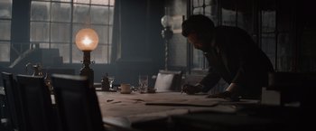 Movie still from “Eiffel” (2021), directed by Martin Bourboulon – A man sitting at a table writing on a piece of paper; Wide shot, Over the shoulder angle