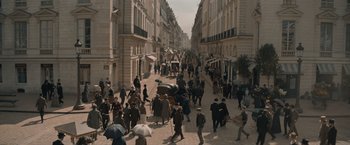 Movie still from “Eiffel” (2021), directed by Martin Bourboulon – A crowd of people walking down a street with umbrellas; Extreme Wide shot, High angle
