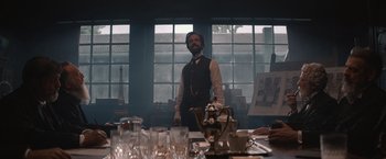 Movie still from “Eiffel” (2021), directed by Martin Bourboulon – A man standing in front of a dining room table; Medium shot, Low angle