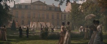 Movie still from “Eiffel” (2021), directed by Martin Bourboulon – Two women are standing in the grass in front of a building; Extreme Wide shot, High angle