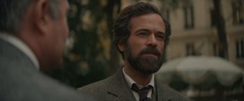 Movie still from “Eiffel” (2021), directed by Martin Bourboulon – A man with a beard wearing a suit and tie; Close Up shot, Over the shoulder angle