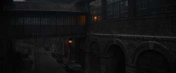Movie still from “Eiffel” (2021), directed by Martin Bourboulon – An old brick building with a street light in the middle of it; Extreme Wide shot, High angle