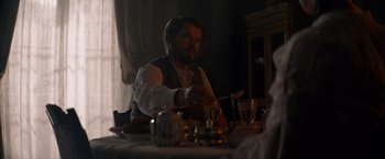 Movie still from “Eiffel” (2021), directed by Martin Bourboulon – A man sitting at a dinner table with a spoon; Medium shot, Over the shoulder angle