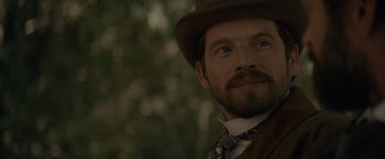 Movie still from “Eiffel” (2021), directed by Martin Bourboulon – A person wearing a hat with trees in the background; Close Up shot, Over the shoulder angle