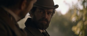 Movie still from “Eiffel” (2021), directed by Martin Bourboulon – A man with a beard wearing a suit and a hat; Close Up shot, Over the shoulder angle