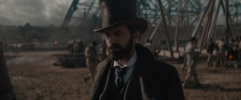 Movie still from “Eiffel” (2021), directed by Martin Bourboulon – A man in a top hat and a long beard; Medium shot, Over the shoulder angle