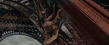 Movie still from “Eiffel” (2021), directed by Martin Bourboulon – A man in a trench coat is working on a metal structure; Wide shot, Low angle