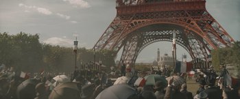 Movie still from “Eiffel” (2021), directed by Martin Bourboulon – A group of people standing under an eiffel tower; Extreme Wide shot, Low angle