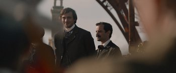 Movie still from “Eiffel” (2021), directed by Martin Bourboulon – A couple of men standing next to each other; Medium shot, Low angle