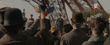 Movie still from “Eiffel” (2021), directed by Martin Bourboulon – A group of people standing in front of an eiffel tower; Extreme Wide shot, Low angle