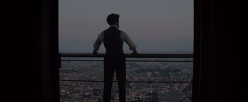 Movie still from “Eiffel” (2021), directed by Martin Bourboulon – A man standing on a ledge looking over a city at night; Medium shot, Low angle