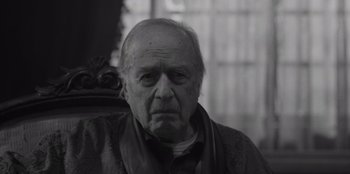 Movie still from “El Conde” (2023), directed by Pablo Larraín – An old man with a beard is sitting in a chair; Close Up shot, Low angle