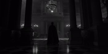 Movie still from “El Conde” (2023), directed by Pablo Larraín – A man in a black cape standing in a dark room; Extreme Wide shot, Low angle