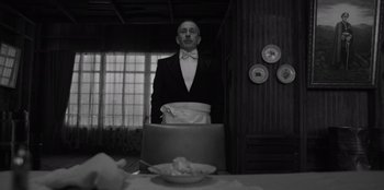 Movie still from “El Conde” (2023), directed by Pablo Larraín – A man standing in front of a table with a bowl on it; Medium shot, Low angle