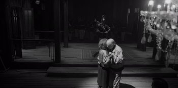 Movie still from “El Conde” (2023), directed by Pablo Larraín – An older couple kissing in front of an orchestra; Wide shot, High angle