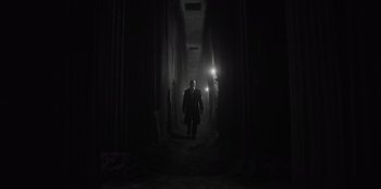 Movie still from “El Conde” (2023), directed by Pablo Larraín – A man walking down a dark hallway in a building; Wide shot, Low angle