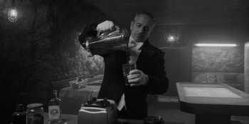 Movie still from “El Conde” (2023), directed by Pablo Larraín – A man pouring a drink into a glass in a black and white photo; Medium shot, Low angle
