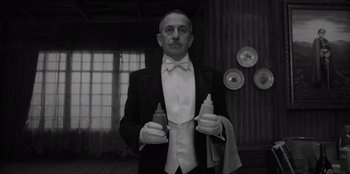 Movie still from “El Conde” (2023), directed by Pablo Larraín – A man in a tuxedo holding two bottles of sauce; Medium shot, Low angle