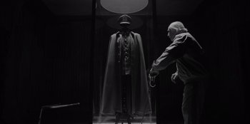 Movie still from “El Conde” (2023), directed by Pablo Larraín – A man is standing in front of a mannequin wearing a cape; Medium shot, Low angle