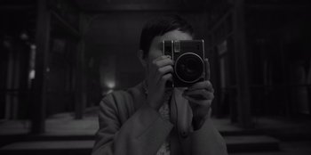 Movie still from “El Conde” (2023), directed by Pablo Larraín – A man taking a picture of himself with a digital camera; Close Up shot, Over the shoulder angle