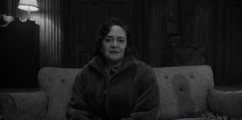 Movie still from “El Conde” (2023), directed by Pablo Larraín – A black and white photo of a woman sitting on a couch; Medium shot, High angle