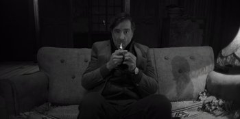 Movie still from “El Conde” (2023), directed by Pablo Larraín – A man sitting on top of a couch with a cigarette in his mouth; Medium shot, Low angle